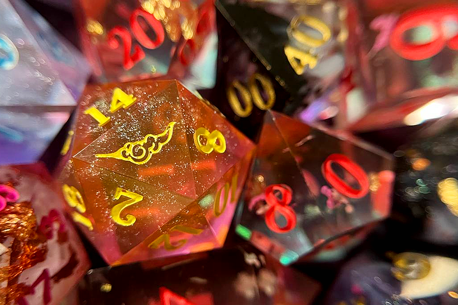 cluster of handmade d&d dice, with a d20 in focus showcasing the sambal & mages logo 